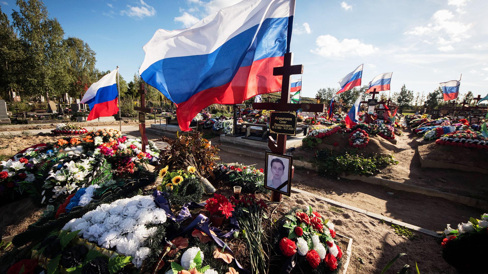 Über frischen Gräbern mit vielen Blumenkränzen und Fotos der verstorbenen wehen weiß-blau-rote Flaggen
