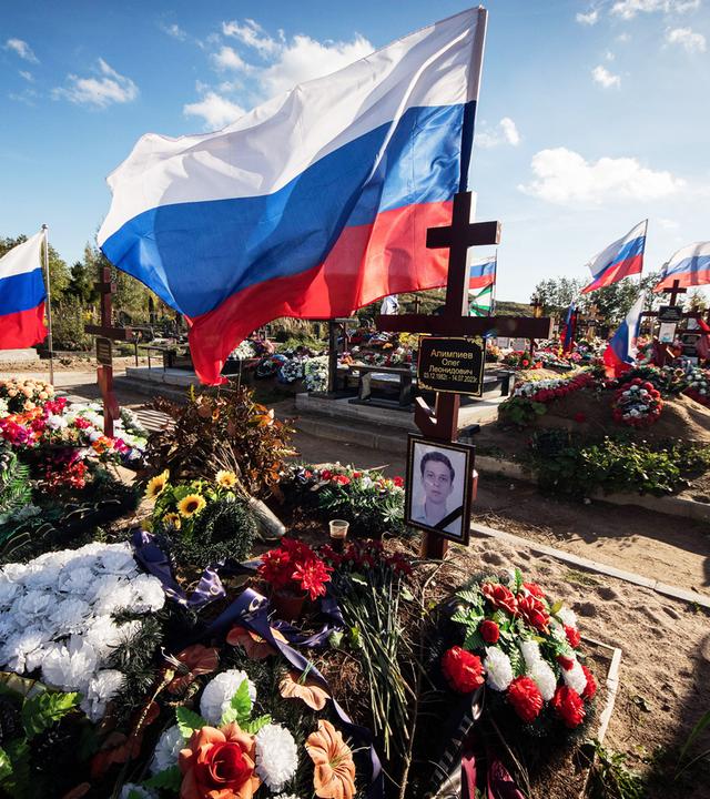 Über frischen Gräbern mit vielen Blumenkränzen und Fotos der verstorbenen wehen weiß-blau-rote Flaggen