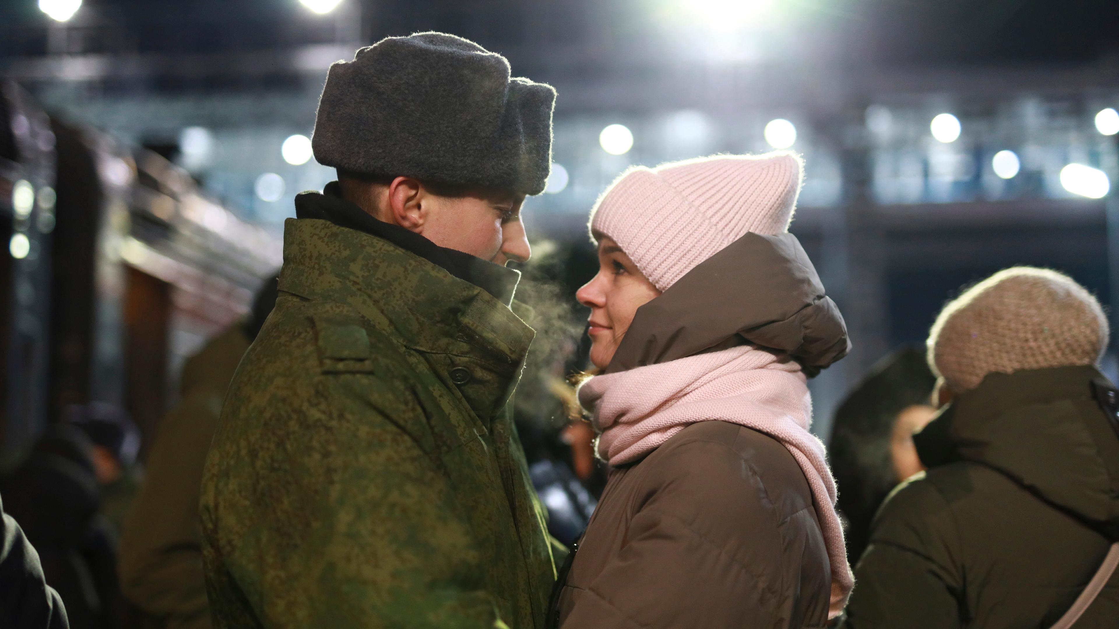 Russischer Soldat umarmt seine Partnerin an einem Bahngleis.