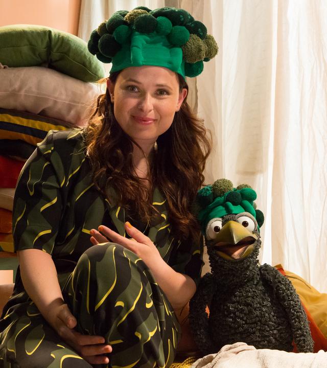 Anna und Rudi sitzen in der Kuschelecke und schauen in die Kamera. Sie tragen beide Hüte, die an Brokkoli erinnern. 