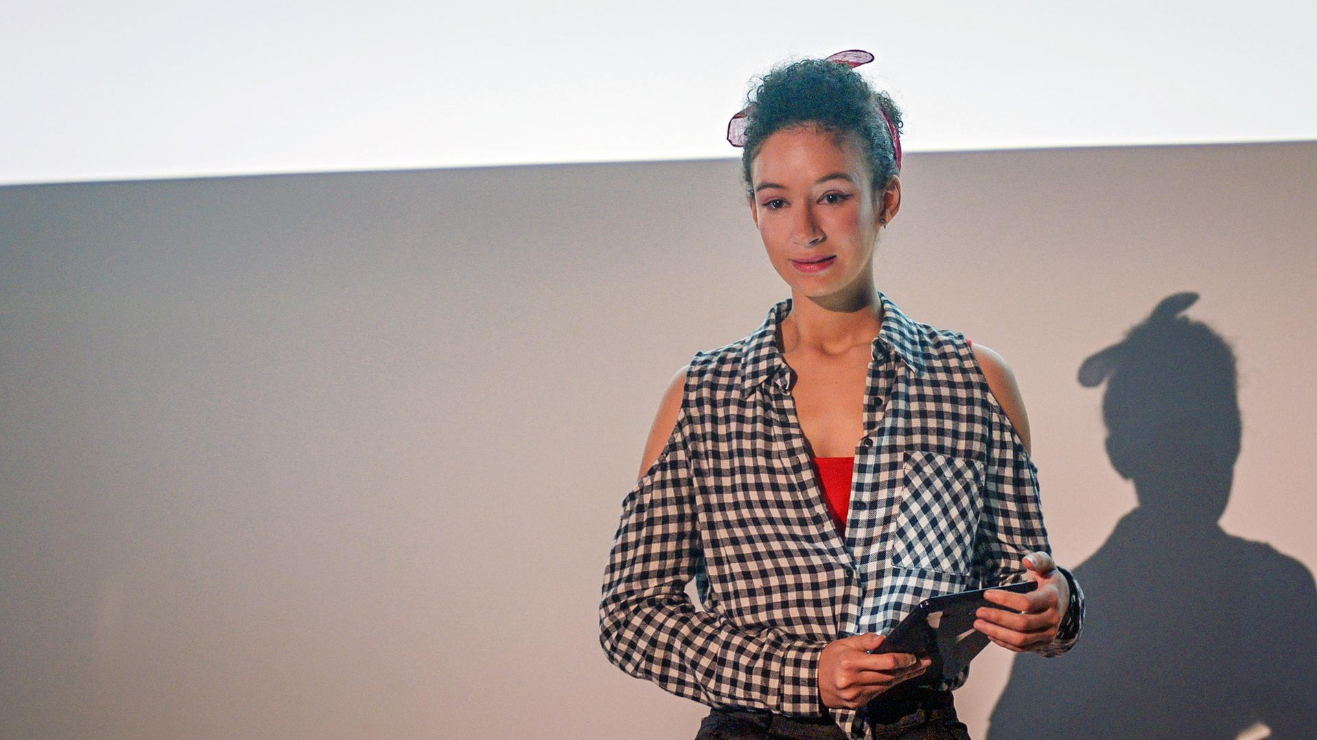 Ines hält ihren Vortrag an einer Pariser Universität. In der Hand hält sie ihre Unterlagen.