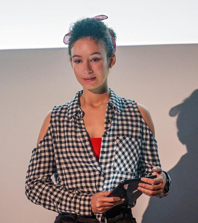 Ines hält ihren Vortrag an einer Pariser Universität. In der Hand hält sie ihre Unterlagen.