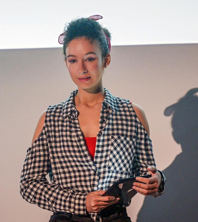 Ines hält ihren Vortrag an einer Pariser Universität. In der Hand hält sie ihre Unterlagen.