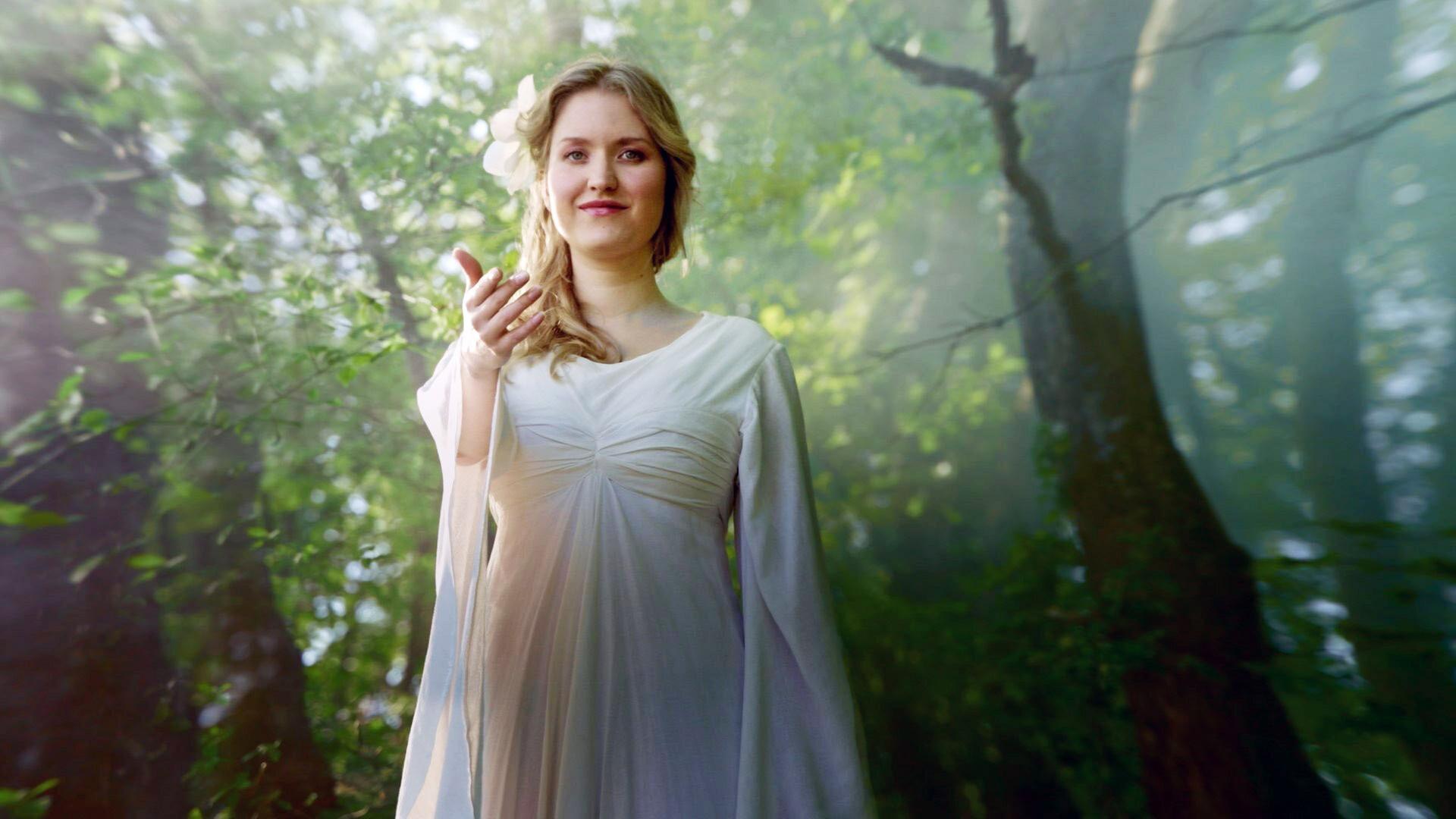 Eine elfenhafte Frau in einem langen weissen Kleid in einem Wald