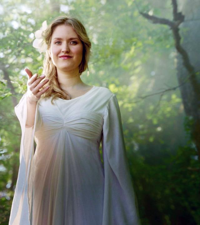 Eine elfenhafte Frau in einem langen weissen Kleid in einem Wald