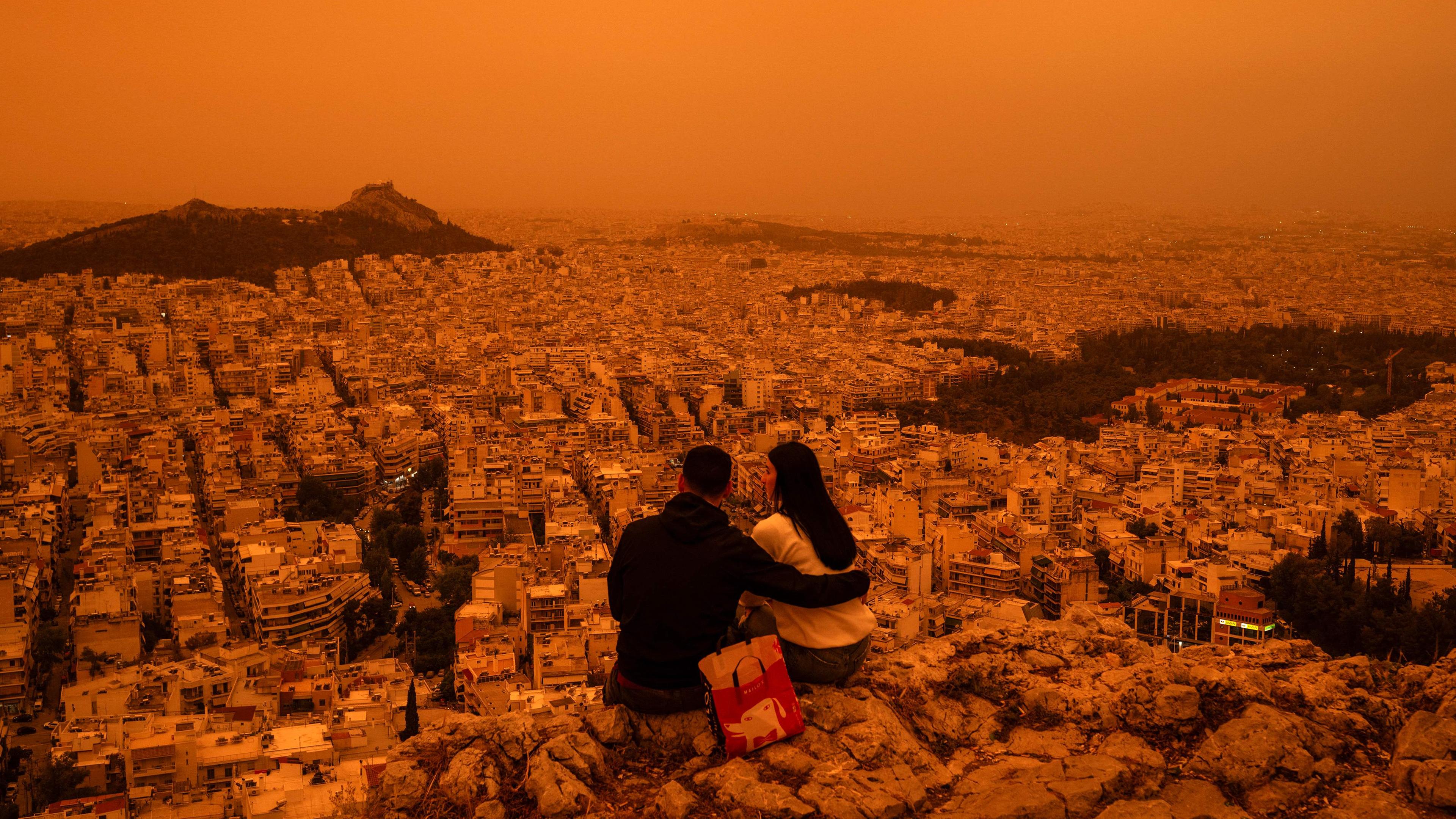 Ein Paar sitzt in Athen auf dem Tourkovounia-Hügel, während Südwinde Wellen von Saharastaub herantragen