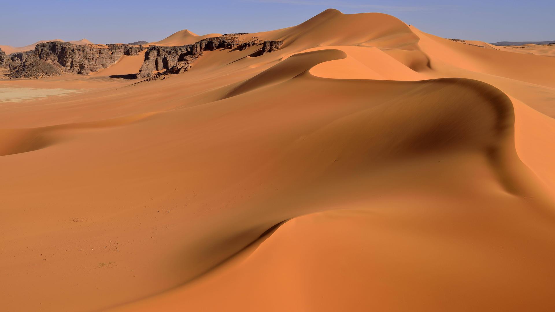 Geschwungene, gelbe Sanddünen, braune Felsen dazwischen.