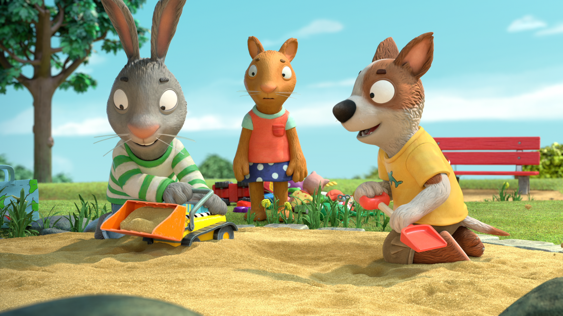 Pip spielt im Sandkasten begeistert mit Zacs Bagger. Zac sitzt rechts von ihm und hat eine Schaufel in der Hand. Hinten steht zwischen den beiden Posy. Sie sieht traurig aus.