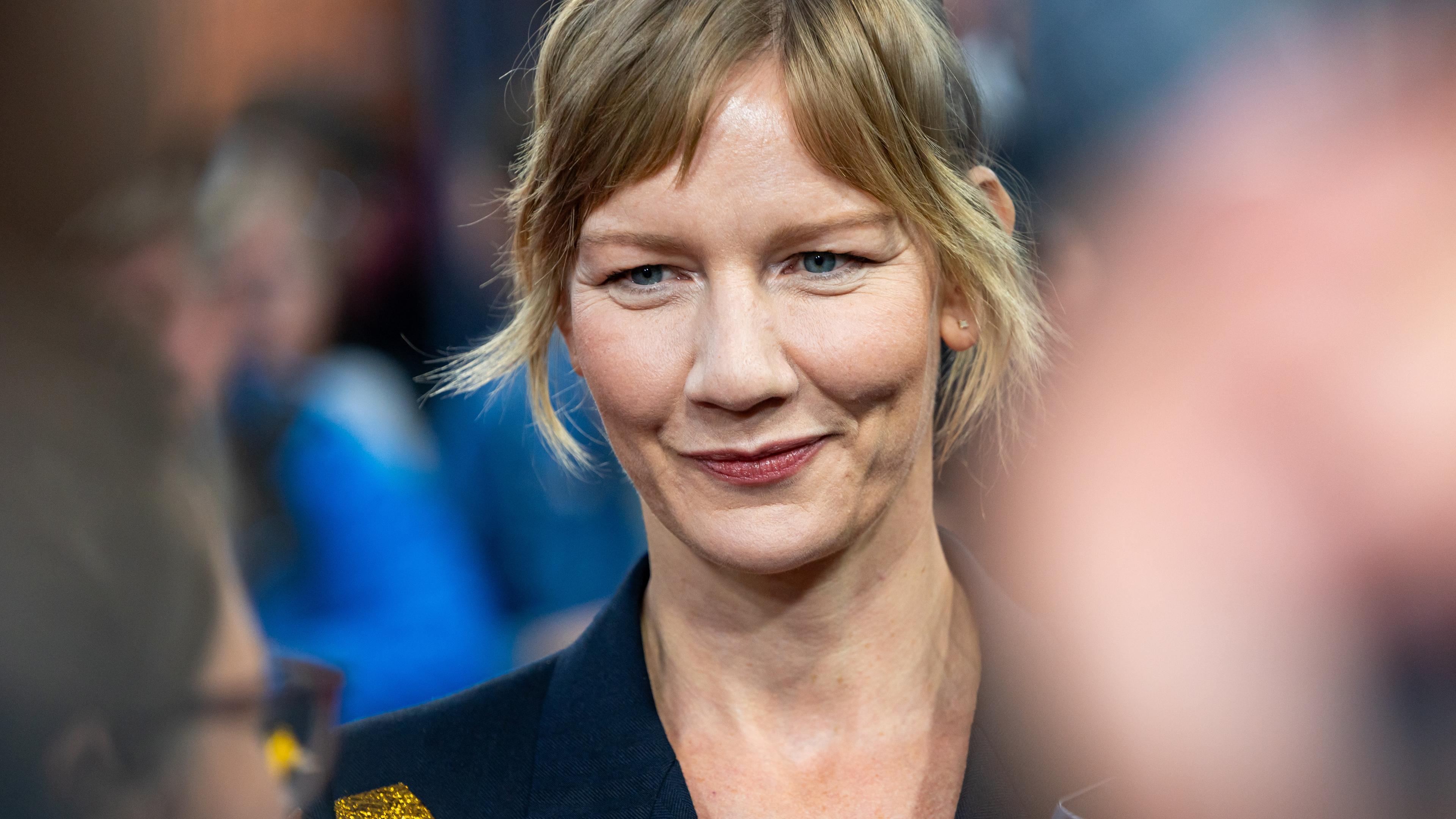 Schauspielerin Sandra Hüller lächelt, umringt von anderen Menschen.
