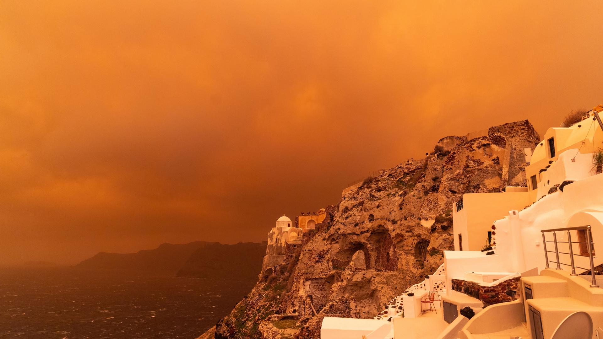 Kräftiger Sturm trägt Sand aus Afrika über die Insel Santorin und färbt den Himmel orangerot ein.