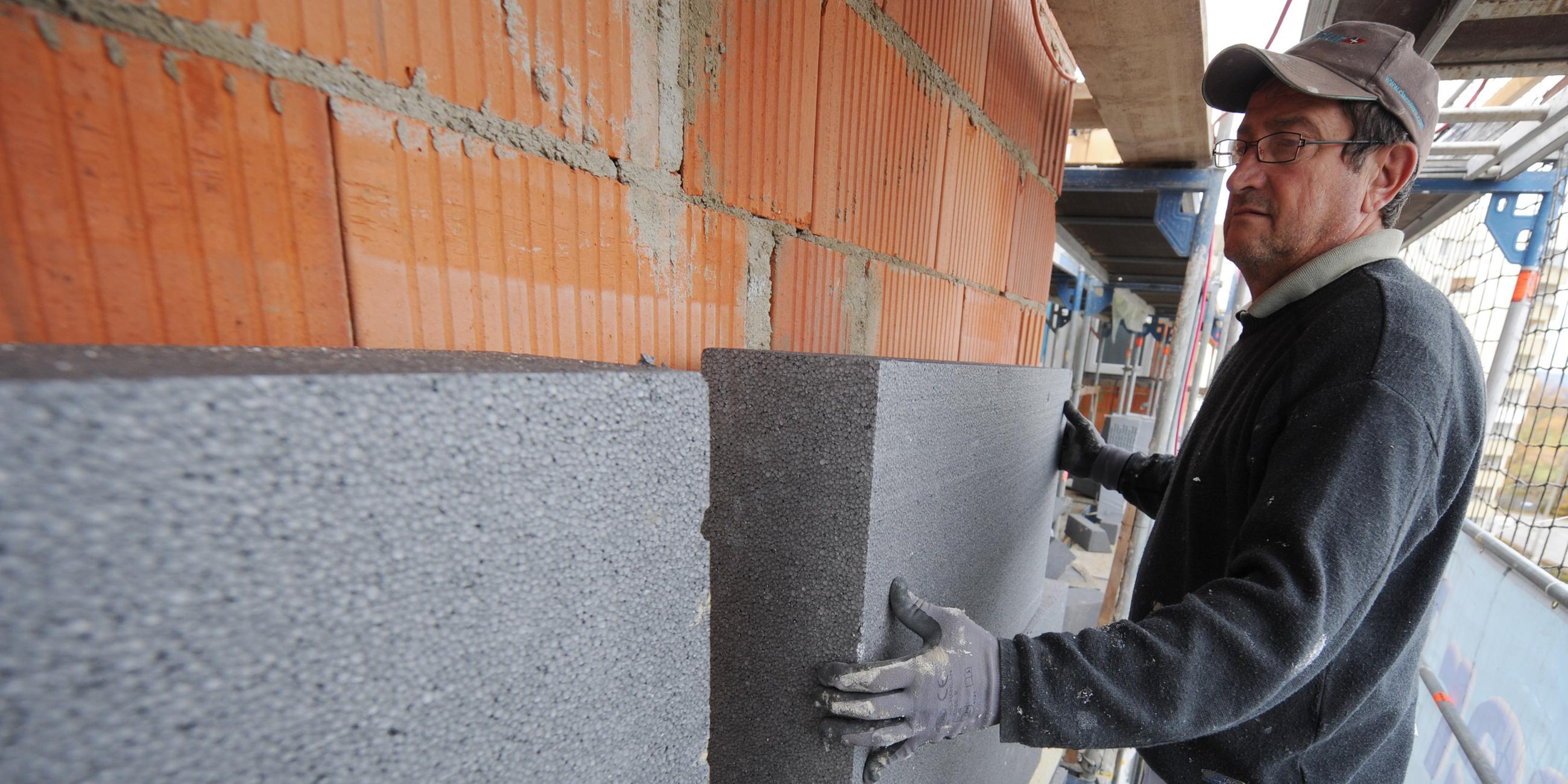 Ein Mann montiert eine Styroporplatte zur Wärmedämmung an die Fassade von einem Mehrfamilienhaus in Straubing (Niederbayern). 