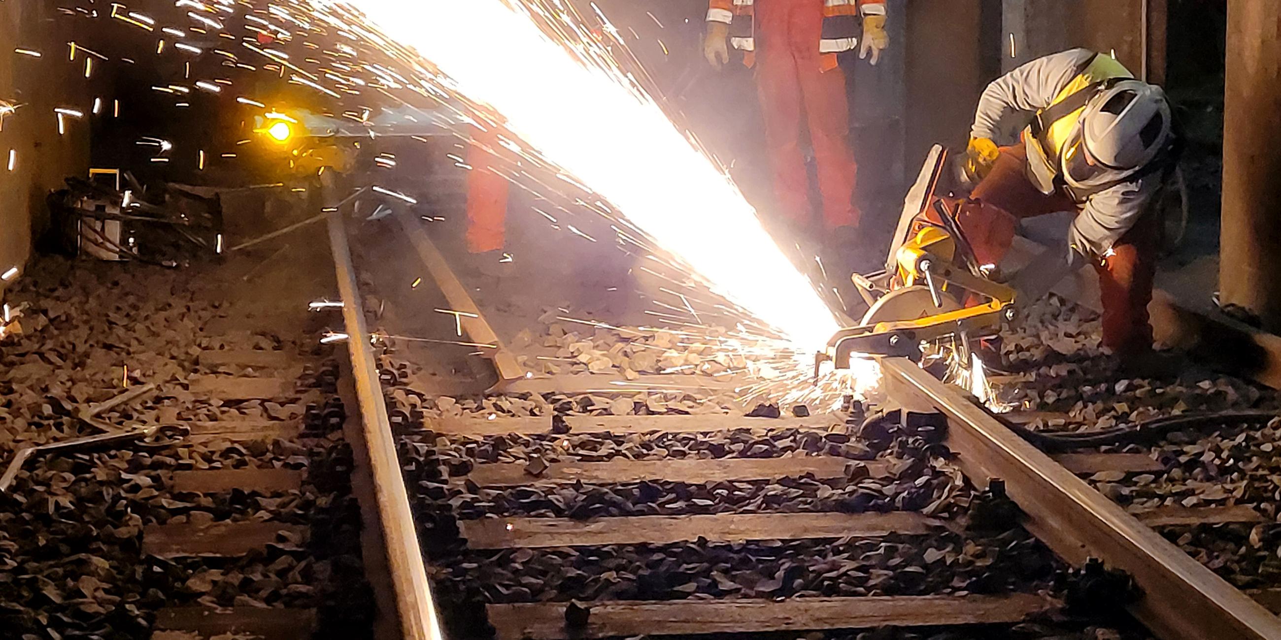 Ein Mann arbeitet an den Schienen im U-Bahn-Tunnel, es fliegen Funken.