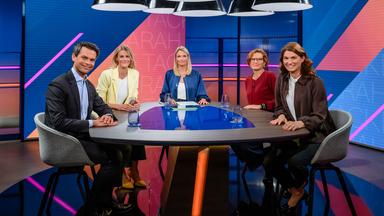 Sarah Tacke und ihre Gäste sitzen an einem Tisch im Studio und schauen in die Kamera.
