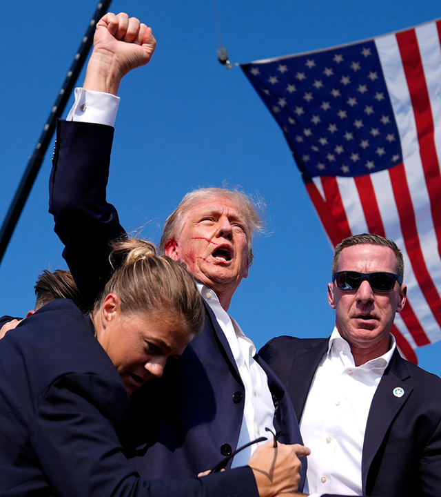 Donald Trump umringt von Sichrheitsleuten hebt die Faust, sein Ohr bluter