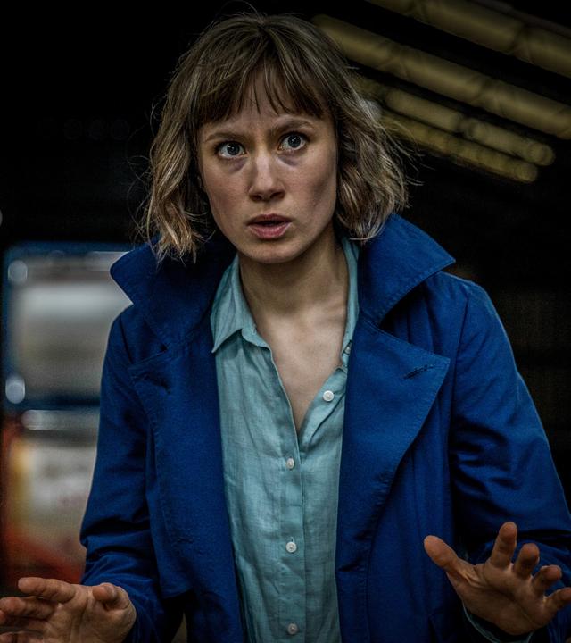 Doro Decker (Alina Levshin) befindet sich in einem dunklen Raum, hat einen blauen Mantel an und hält die flachen, ausgestreckten Hände vor sich.