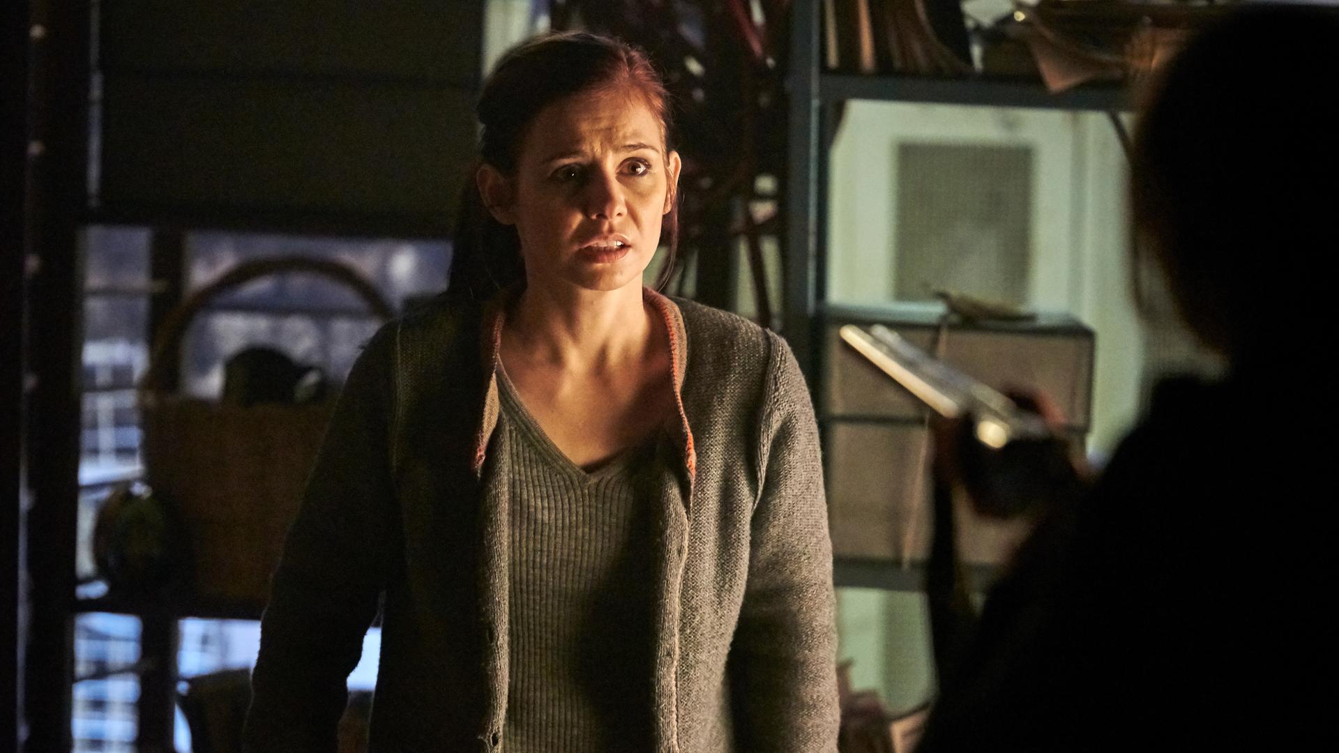 "Schattengrund": Nicola Wagner (Josefine Preuß) steht im Keller und sieht verängstigt zu der Frau, die vor ihr steht. Diese ist nur unscharf von hinten zu sehen, wie sie eine Waffe auf Nicola richtet.