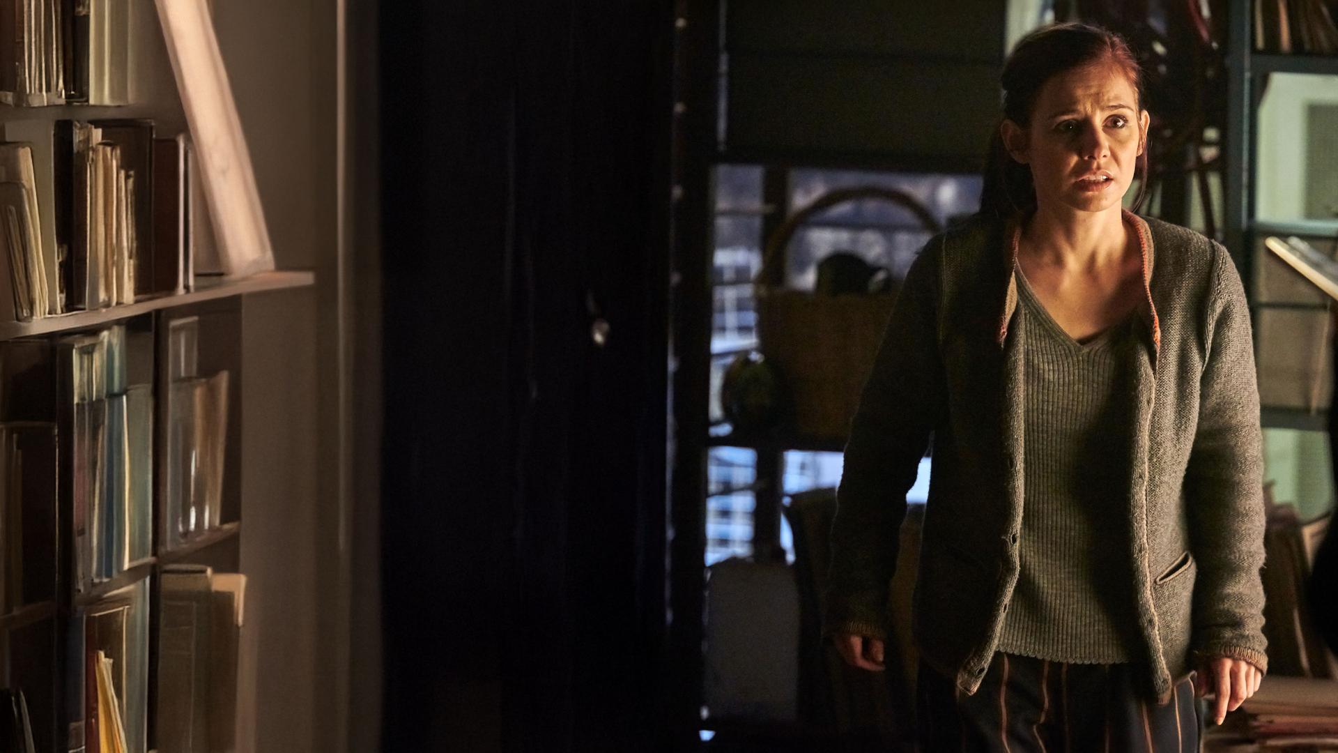 "Schattengrund": Nicola Wagner (Josefine Preuß) steht im Keller und sieht verängstigt zu der Frau, die vor ihr steht. Diese ist nur unscharf von hinten zu sehen, wie sie eine Waffe auf Nicola richtet.