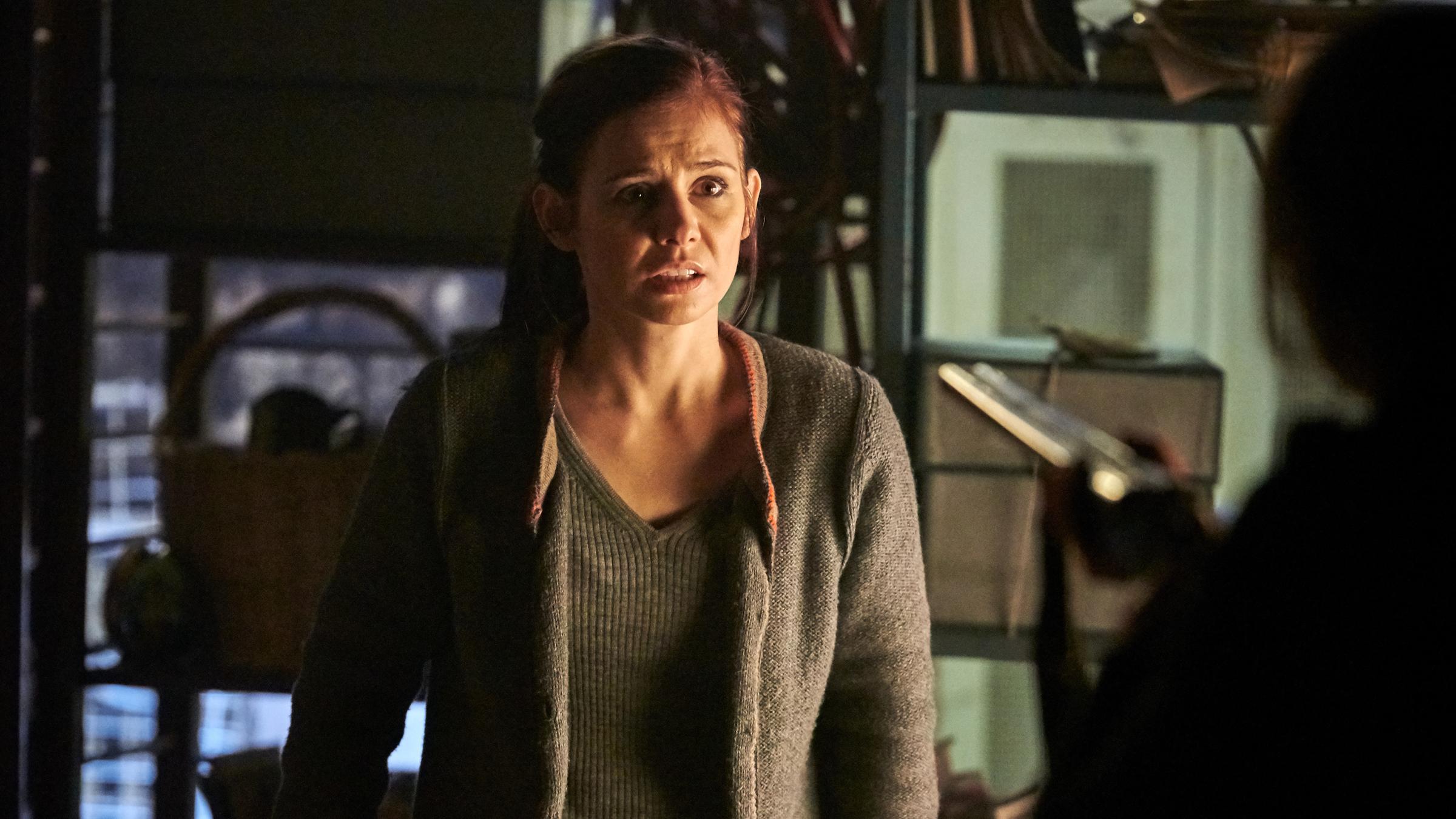 "Schattengrund": Nicola Wagner (Josefine Preuß) steht im Keller und sieht verängstigt zu der Frau, die vor ihr steht. Diese ist nur unscharf von hinten zu sehen, wie sie eine Waffe auf Nicola richtet.