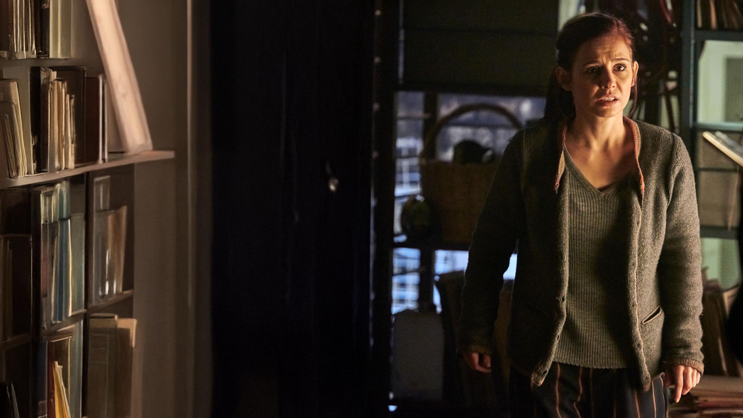 "Schattengrund": Nicola Wagner (Josefine Preuß) steht im Keller und sieht verängstigt zu der Frau, die vor ihr steht. Diese ist nur unscharf von hinten zu sehen, wie sie eine Waffe auf Nicola richtet.