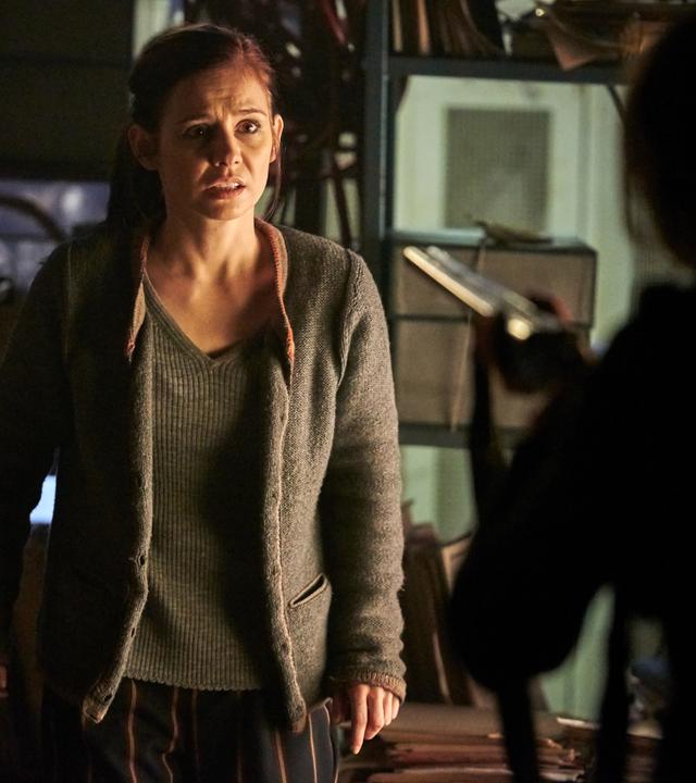 "Schattengrund": Nicola Wagner (Josefine Preuß) steht im Keller und sieht verängstigt zu der Frau, die vor ihr steht. Diese ist nur unscharf von hinten zu sehen, wie sie eine Waffe auf Nicola richtet.