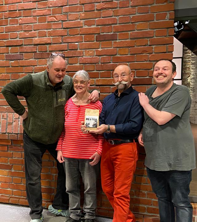 Waldi und Horst Lichter stehen mit zwei Kandidaten von "Bares für Rares" im Studio vor der Backsteinwand. Links ist das "Bares für Rares"-Logo zu sehen.