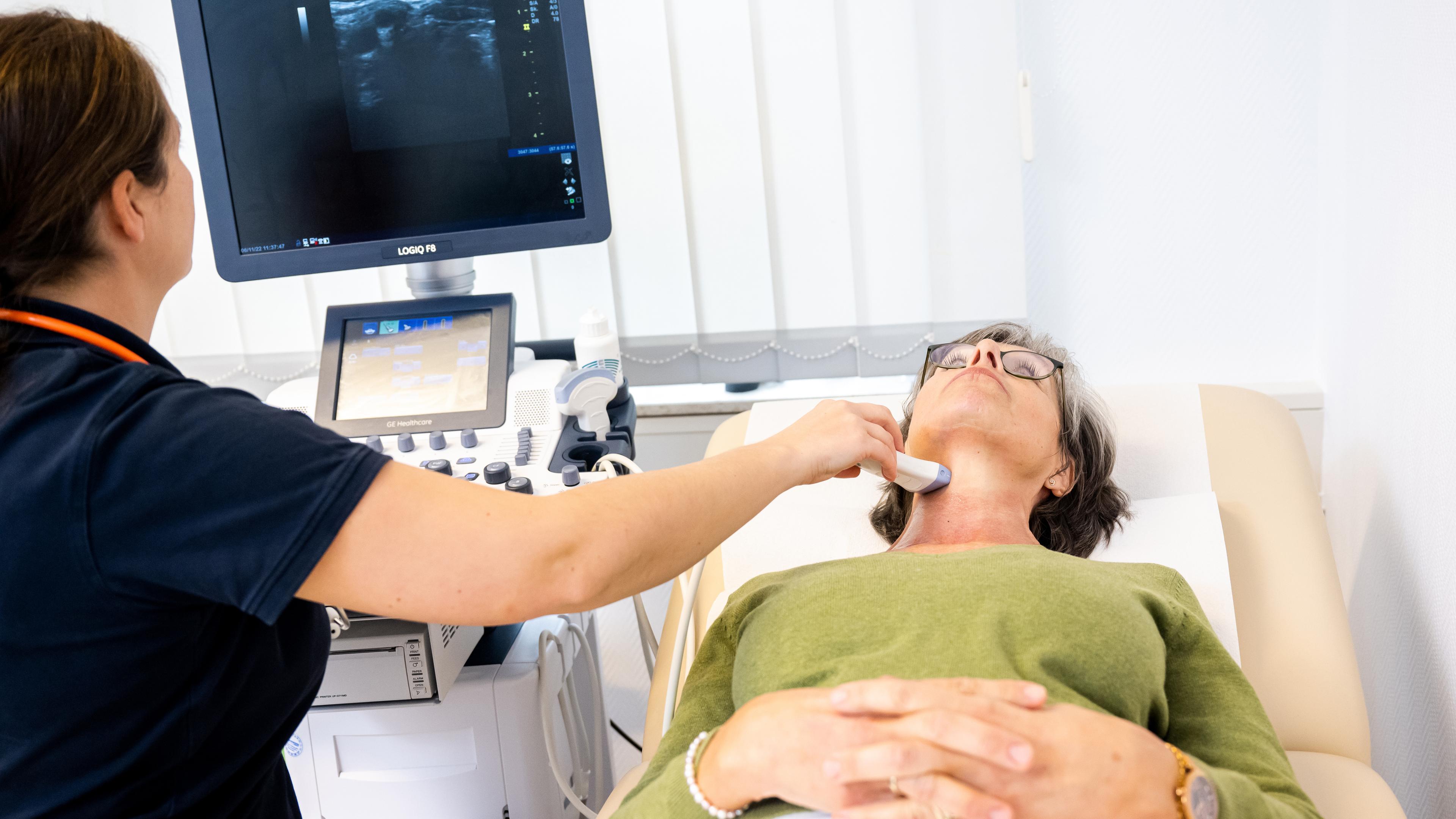 Eine Frau, die auf einer Behandlungsliege liegt, erhält eine Ultraschalluntersuchung der Schilddrüse.