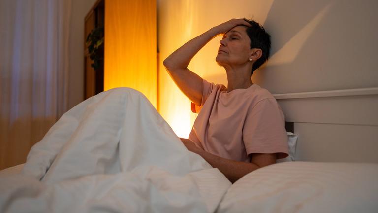 Eine erschöpfte, nachdenkliche ältere Frau mit Schlafstörungen sitzt mit müdem Gesichtsausdruck im Bett.
