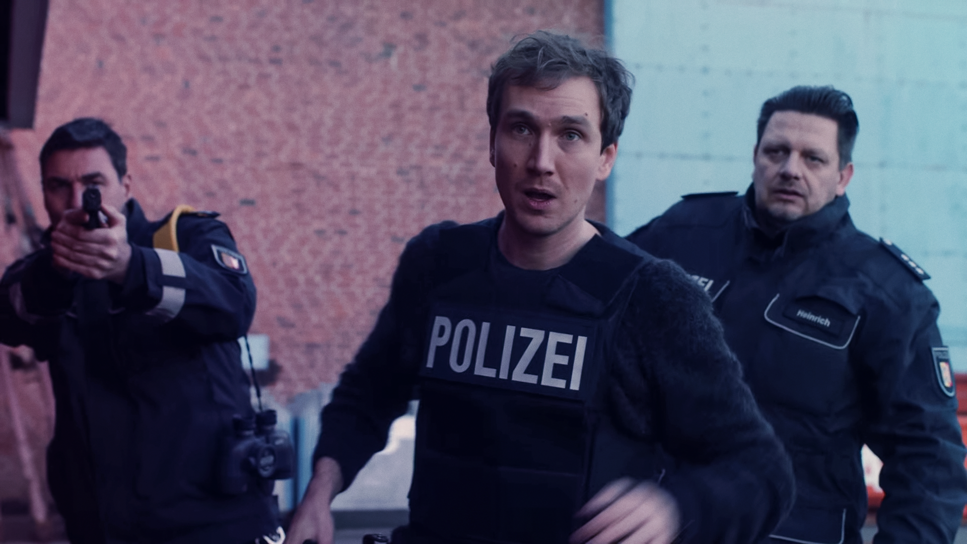 Simon (Jan Krauter) im Einsatz mit schusssicherer Polizeiweste. Hinter ihm zwei Kollegen. 