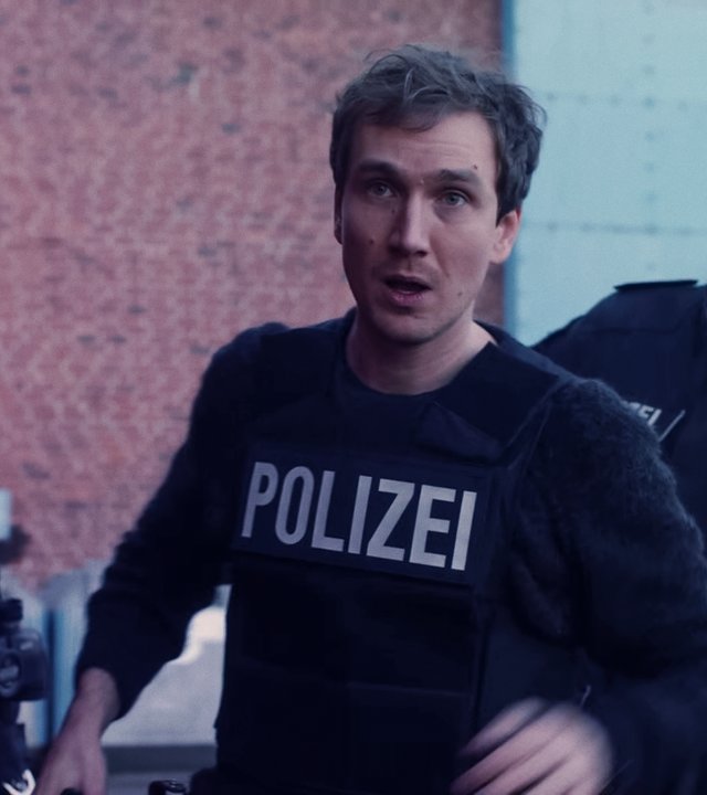 Simon (Jan Krauter) im Einsatz mit schusssicherer Polizeiweste. Hinter ihm zwei Kollegen. 