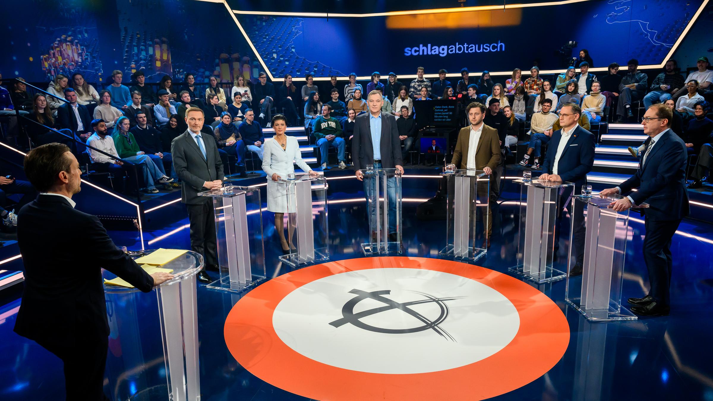 "Schlagabtausch": V.l. Andreas Wunn, Christian Lindner, Sahra Wagenknecht, Jan van Aken, Felix Banaszak, Tino Chrupalla, Alexander Dobrindt stehen im Halbkreis im Studio an Pulten. Im Hintergrund Studiopublikum