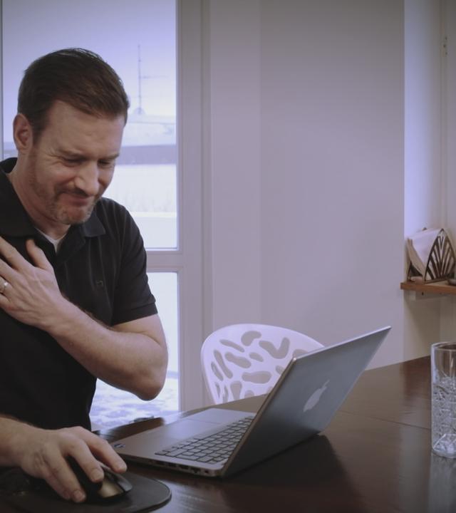 Mann fasst sich schmerzverzerrt an seine Schulter