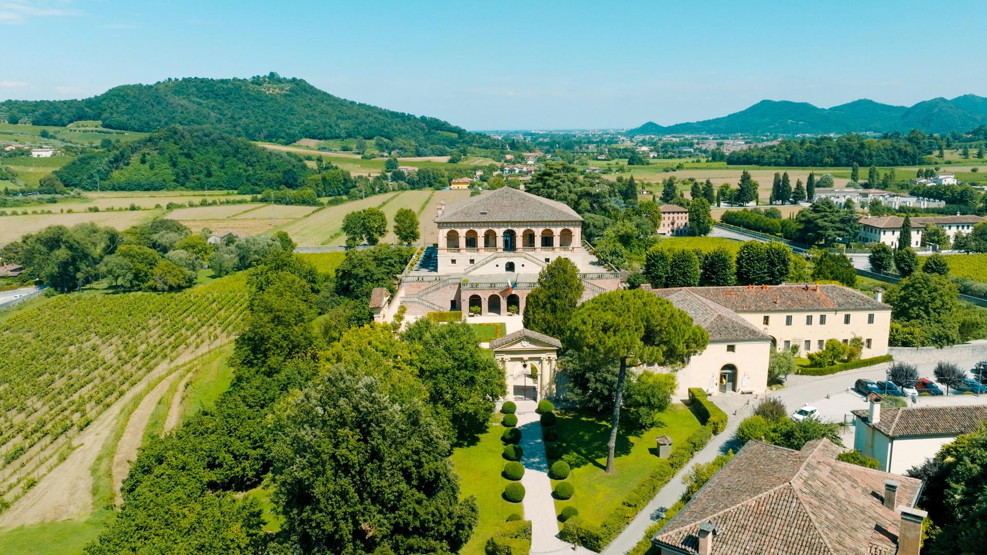 Die Villa Vescovi liegt eingebettet in die Weinlandschaft der Euganeischen Hügel. Das historische Gebäude mit seiner markanten Loggia thront inmitten gepflegter Gartenanlagen, umgeben von sanften Hügeln und grüner Vegetation.