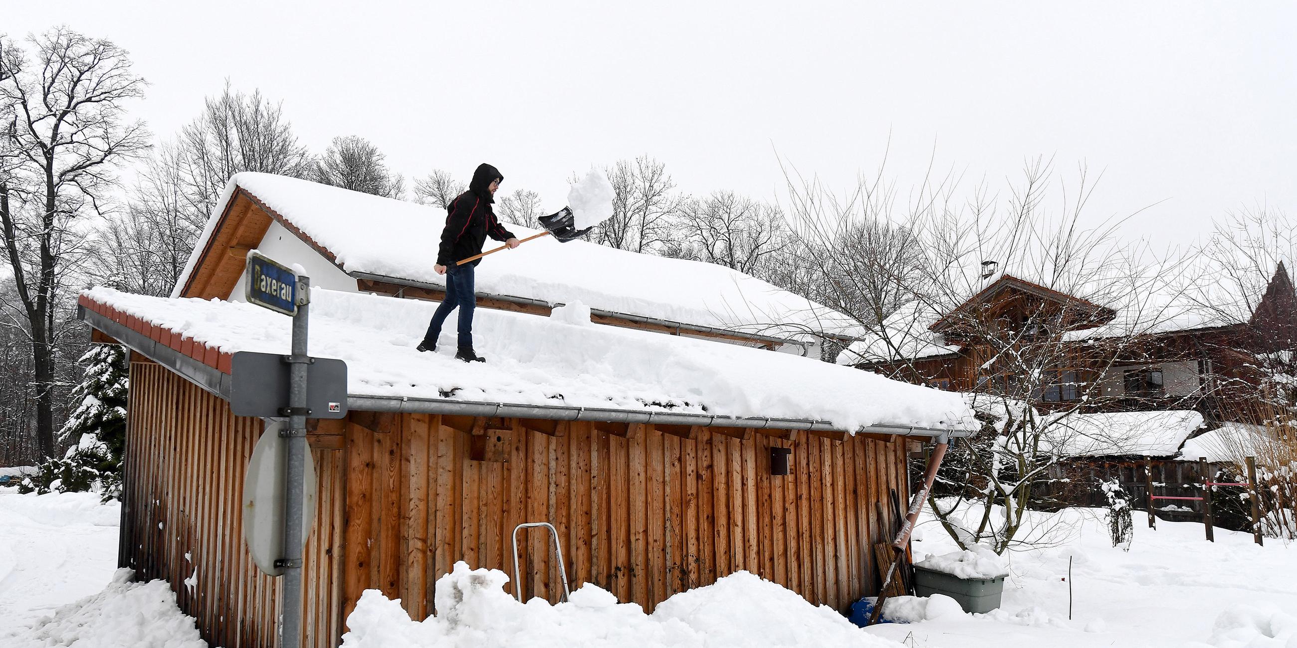 Ein Mann befreit ein Dach vom Schnee.