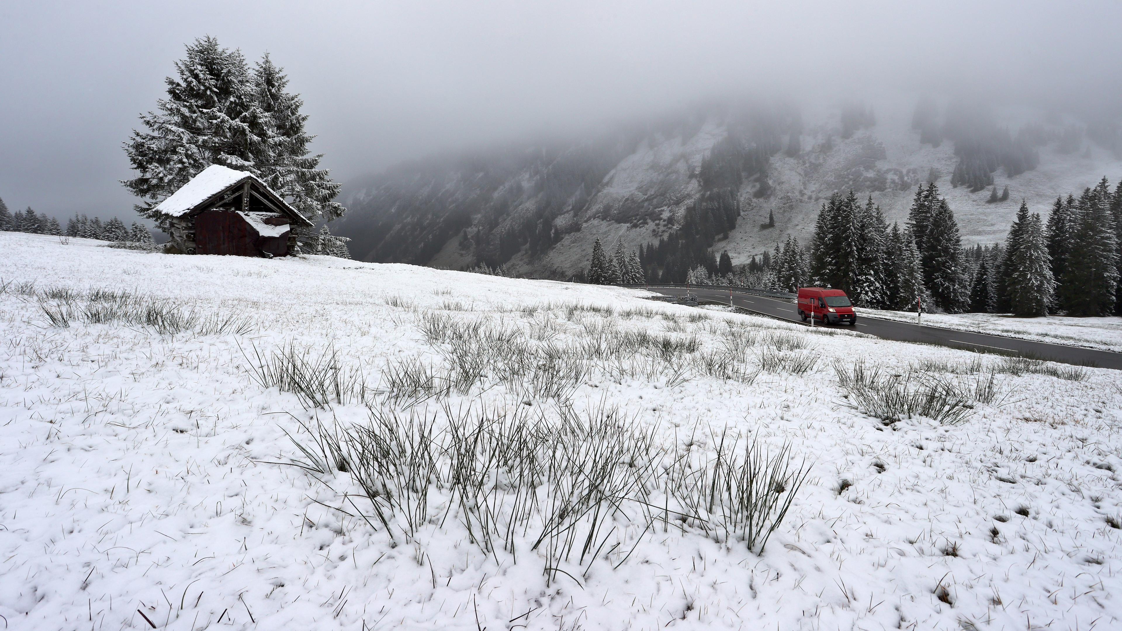 Bayern, Obermaiselstein: Ein Auto fährt am Riedbergpass durch die mit Neuschnee bedeckte Landschaft. 