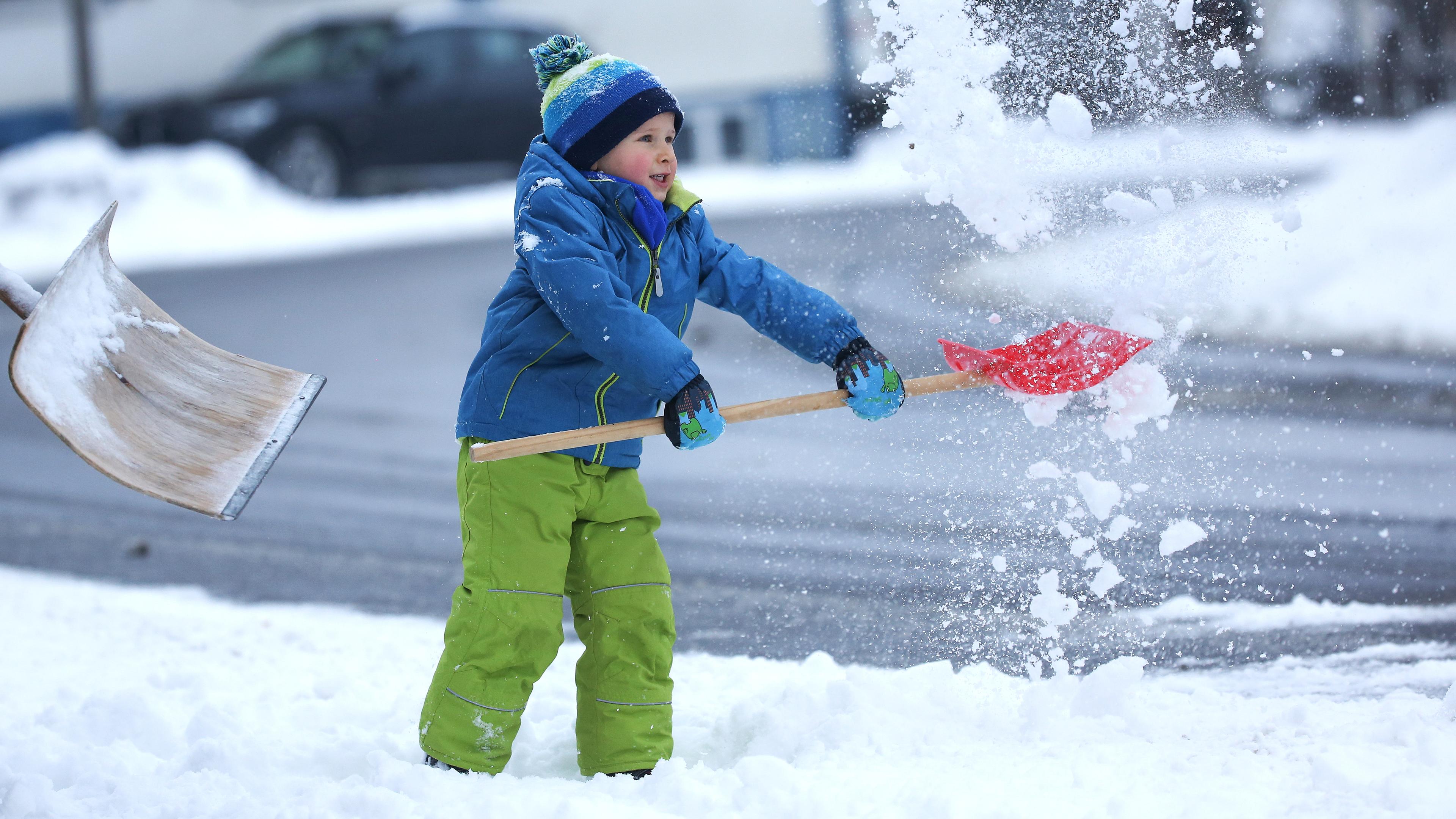 Ein Kind schippt mit einer Schneeschaufel Schnee in die Luft