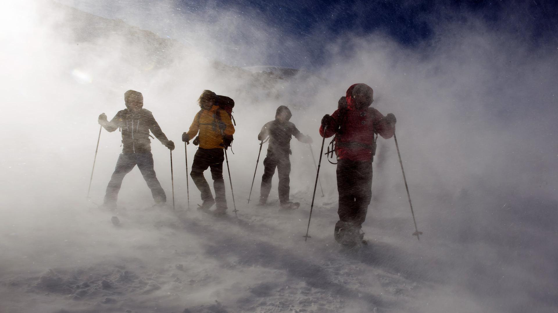 "Die Bergretter - Schneeblind (1)": Vier Männer auf Skiern stehen in einer Wolke aus Pulverschnee auf der Piste.