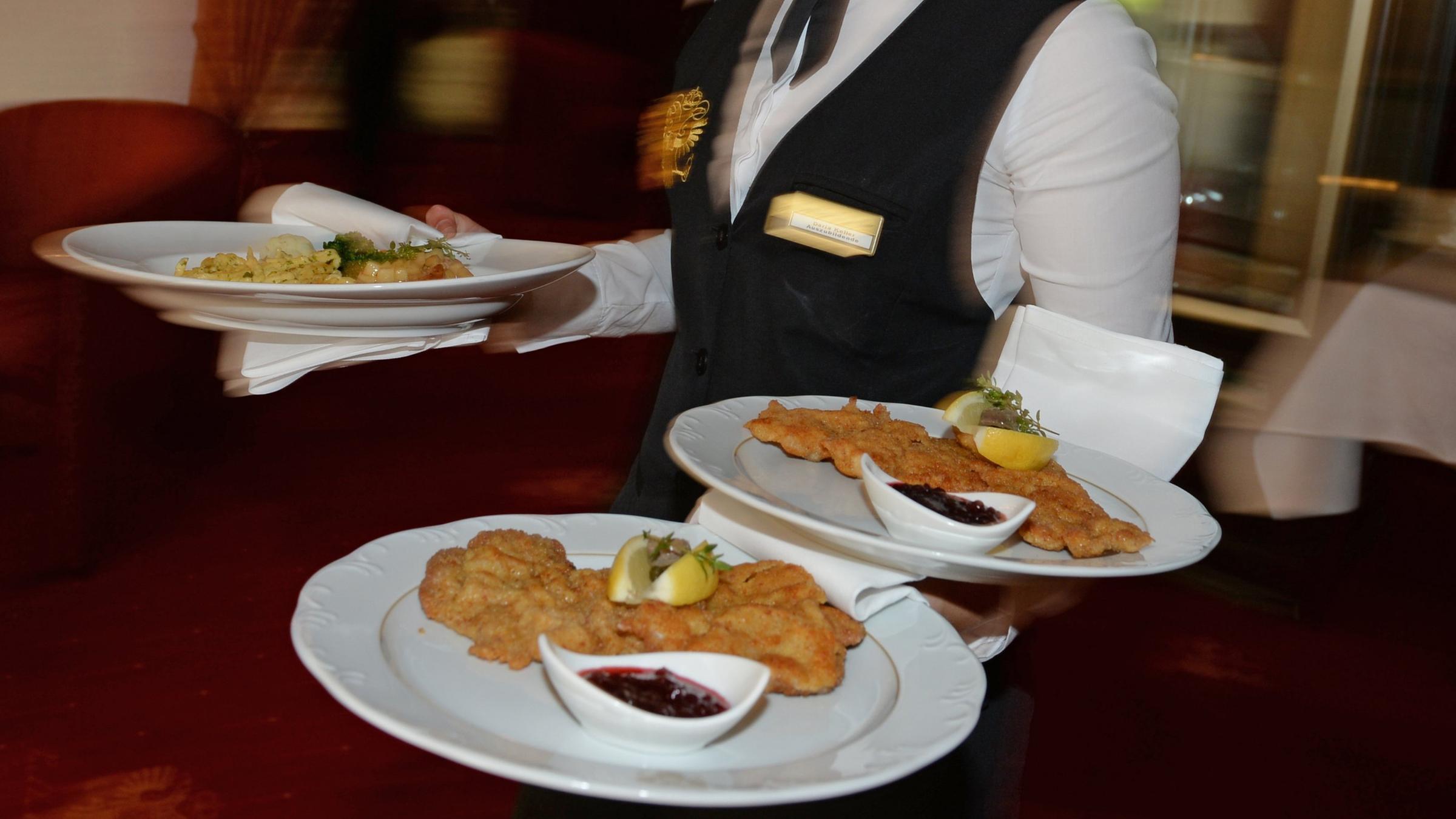 Ein Kellner serviert in einem Restaurant Teller mit Schnitzeln