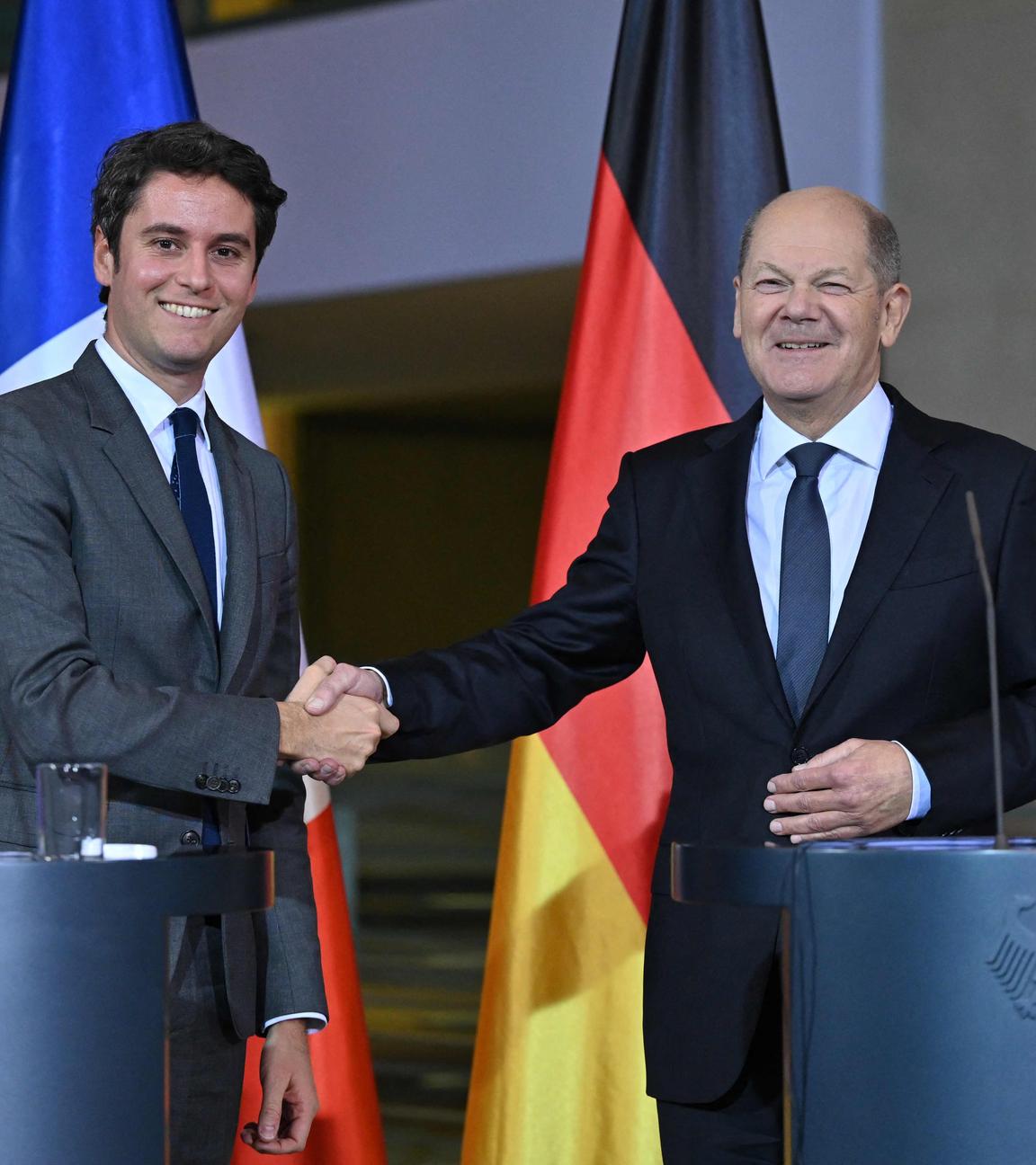 Bundeskanzler Olaf Scholz und Frankreichs Premierminister Gabriel Attal beim Treffen in Berlin. Sie stehen hinter zwei Redepulten und schütteln lächelnd die Hände.