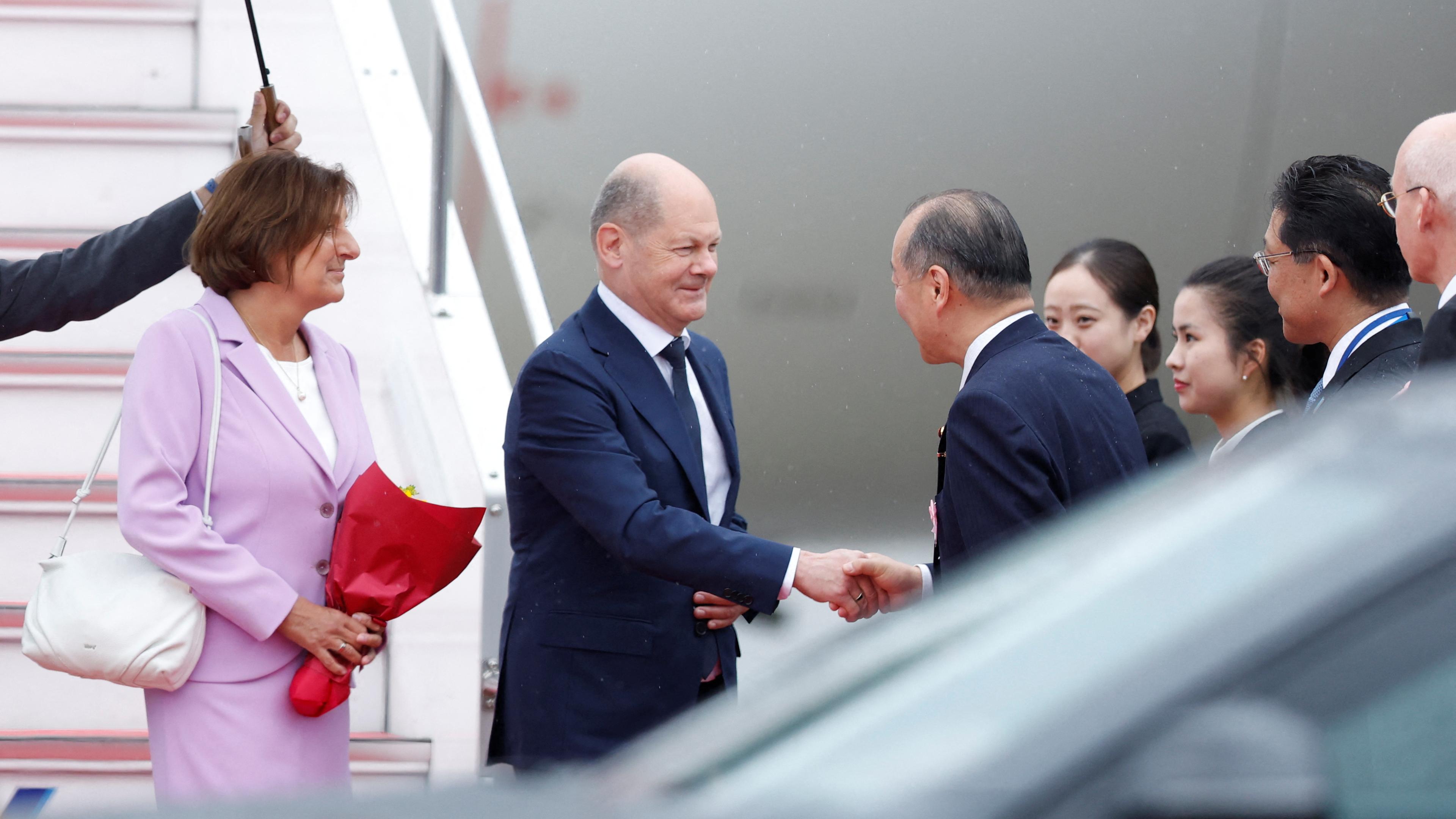 Bundeskanzler Scholz und seine Frau werden am Flughafen in Hiroshima von einem Empfangskommittee begrüßt