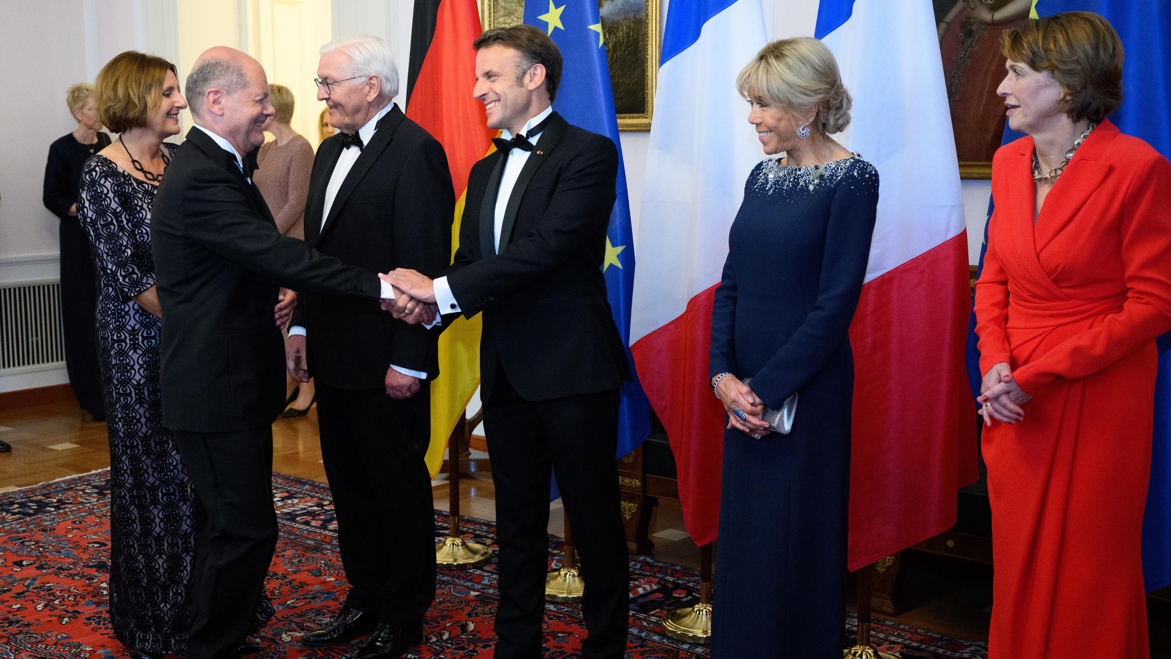 Kanzler Olaf Scholz und Frankreichs Präsident Emmanuel Macron begrüßen sich beim Defilee im Schloss Bellevue