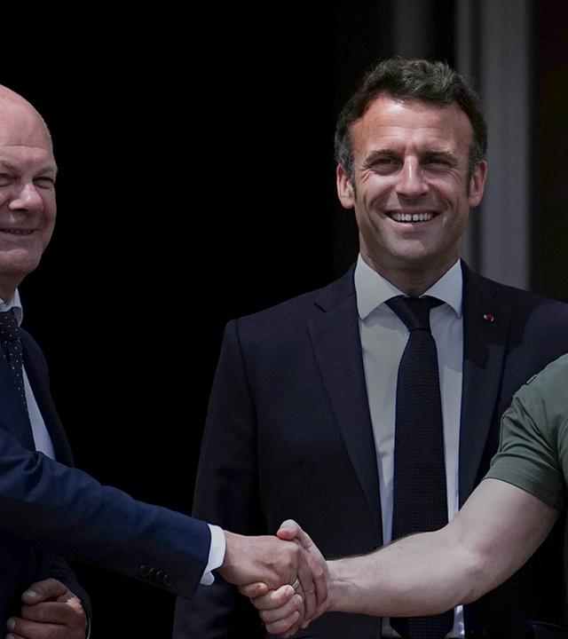 Zu sehen sind von links nach rechts, Bundeskanzler Scholz, Frankreichs Präsident Macron und der Präsidenten Selenskyj in Kiew. Scholz und Selenskyj reichen sich die Hand, Macron steht in der mitte hinter den Beiden.