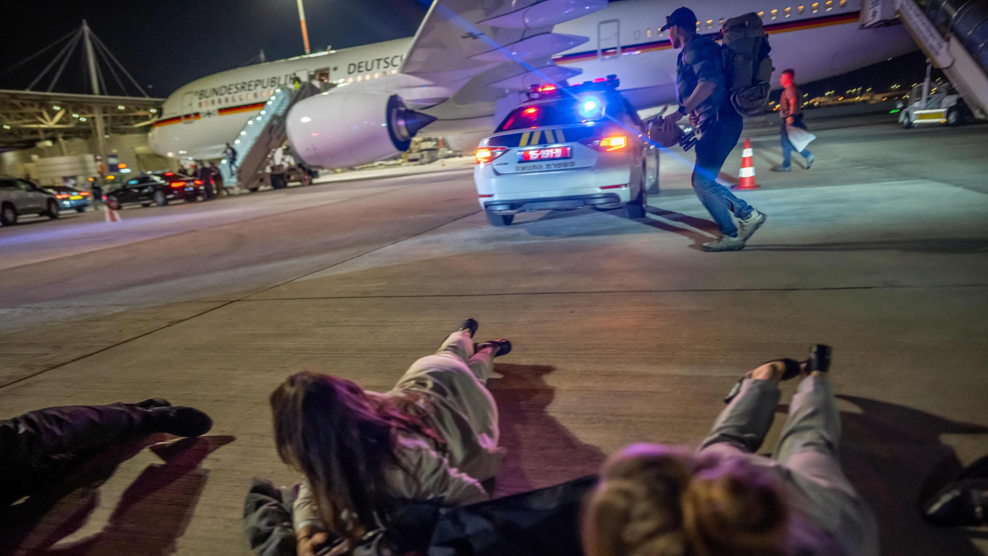Personen liegen auf dem Flughafen von Tel Aviv vor dem Luftwaffen-Airbus von Bundeskanzler Scholz auf dem Boden.