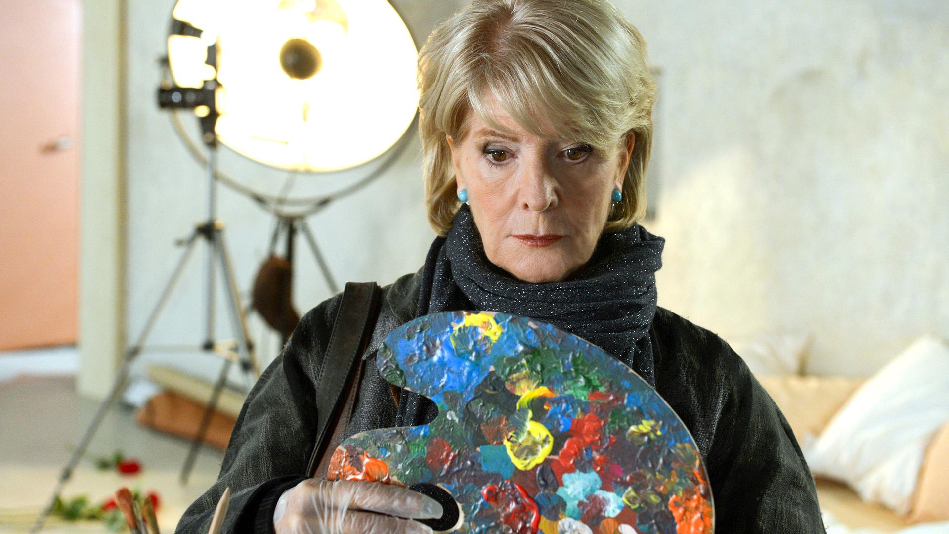 Die Darstellerin schaut bestürzt auf eine Malerpalette