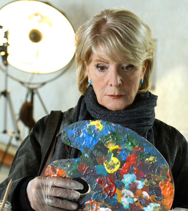 Die Darstellerin schaut bestürzt auf eine Malerpalette