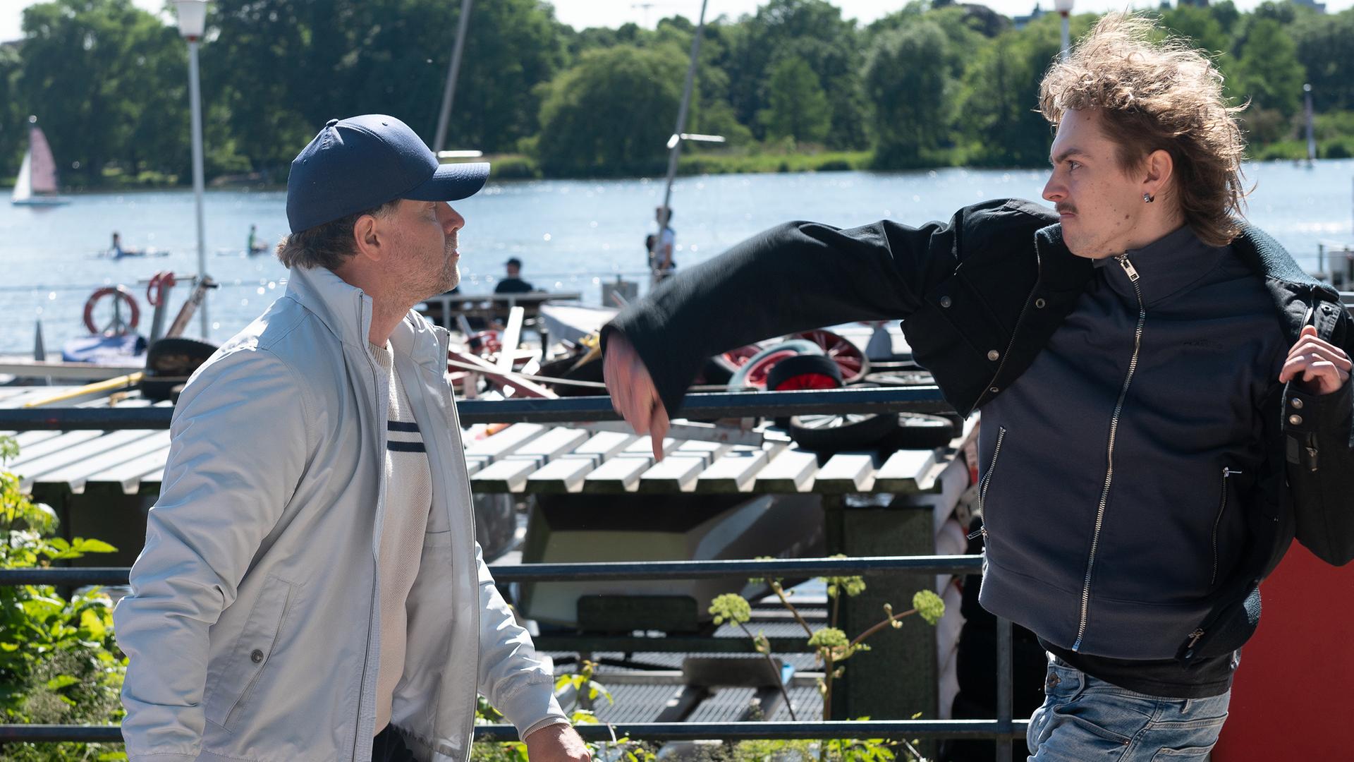 An der Außenalster: Kevin (Cedric Eich) ist im Begriff mit seiner rechten Faust Sebastian Matthiesen (Janek Rieke) zu schlagen, der verdutzt vor ihm steht.