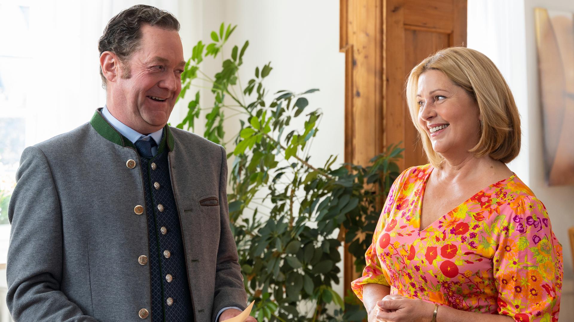  Bürgermeister Schretzmayer (Jürgen Tonkel) und Marie Hofer stehen sich im Büro lächelnd gegenüber. Schretzmayer hält Unterlagen in den Händen.