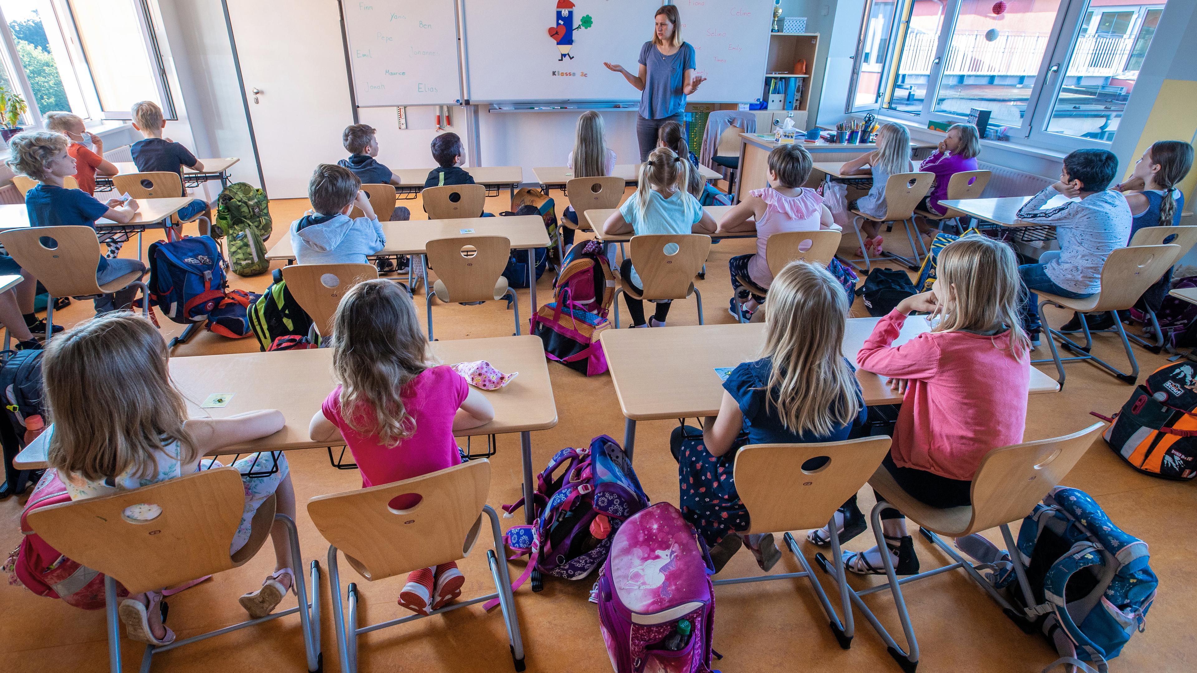 Schüler sitzen in einem Klassenzimer, während die Lehrerin vorne an der Tafel etwas erklärt.