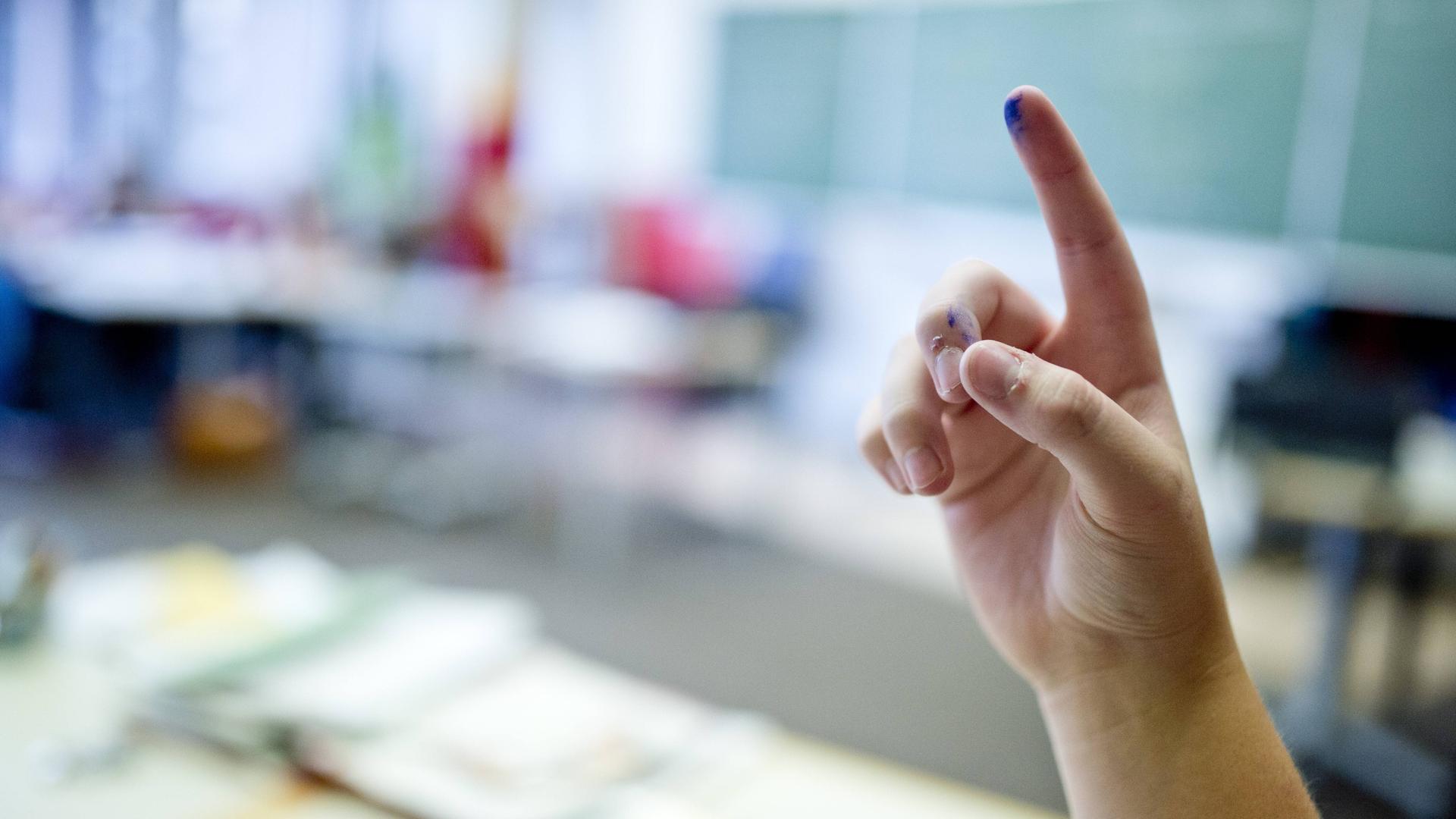 Schüler meldet sich mit hoch gestrecktem Finger im Klassenzimmer.
