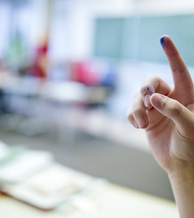 Schüler meldet sich mit hoch gestrecktem Finger im Klassenzimmer.