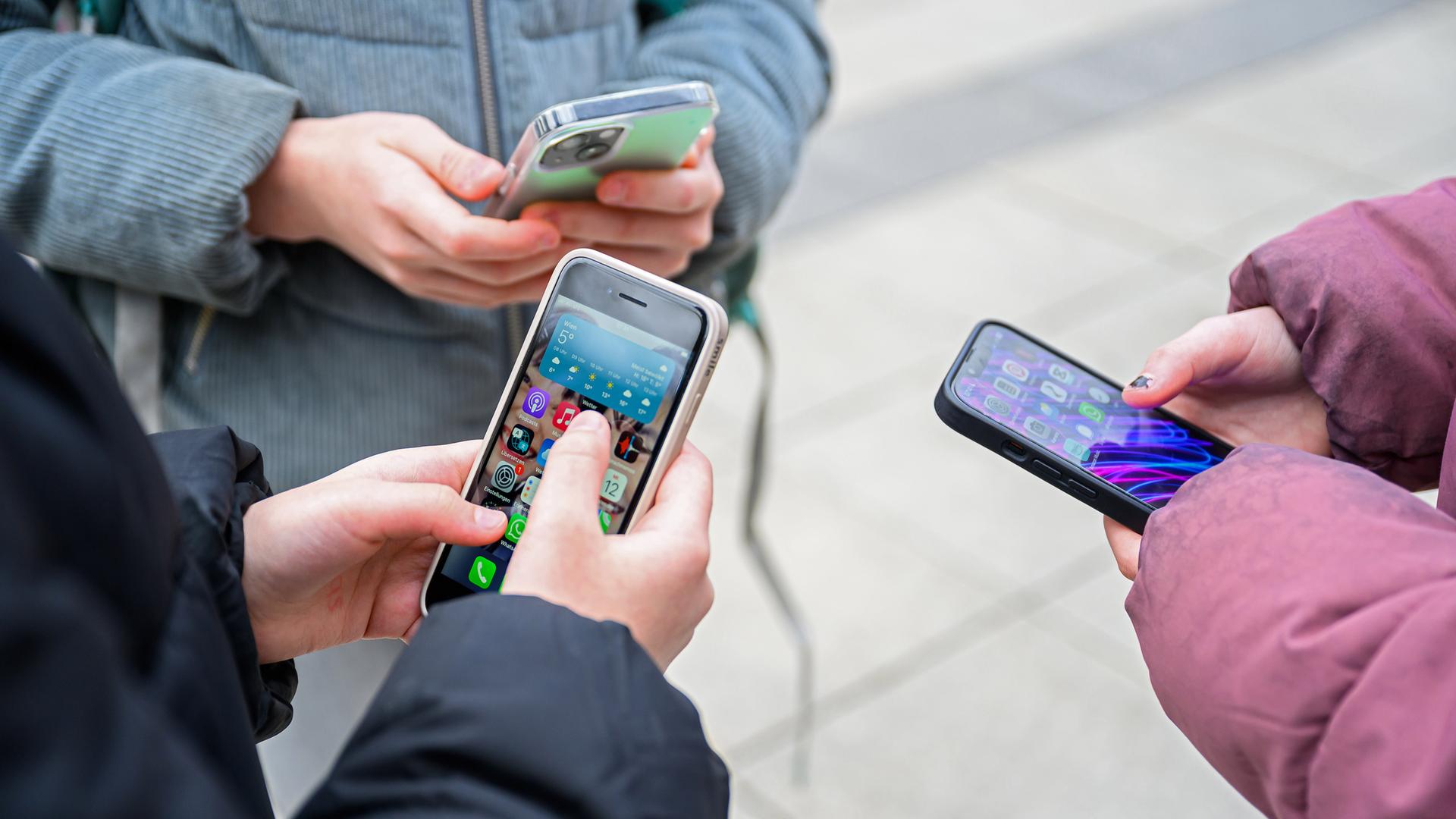 Drei Schülerinnen stehen mit Handys beisammen.